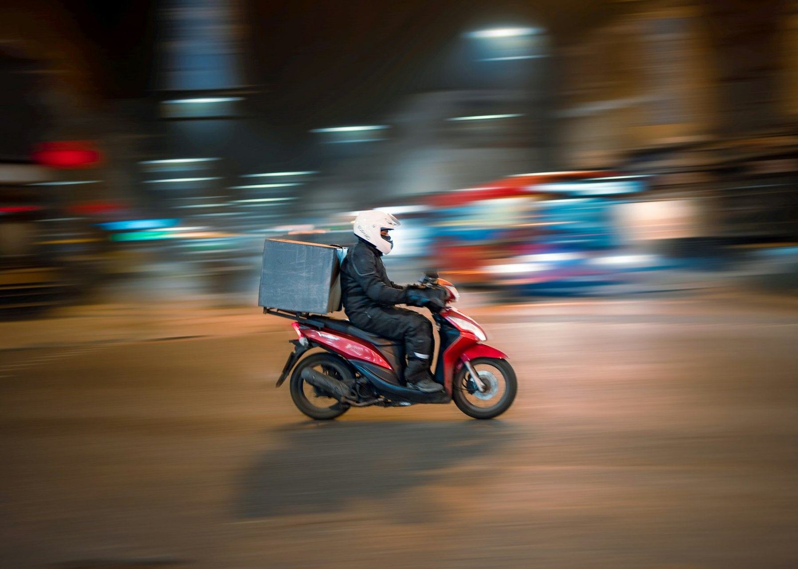 Pengantar motor membawa kotak pesanan di jalan pada malam hari